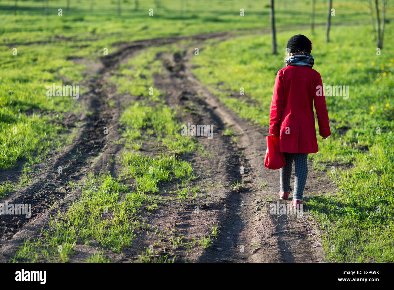 Girl in red coat aller loin par dirty country road, selective focus on girl Banque D'Images