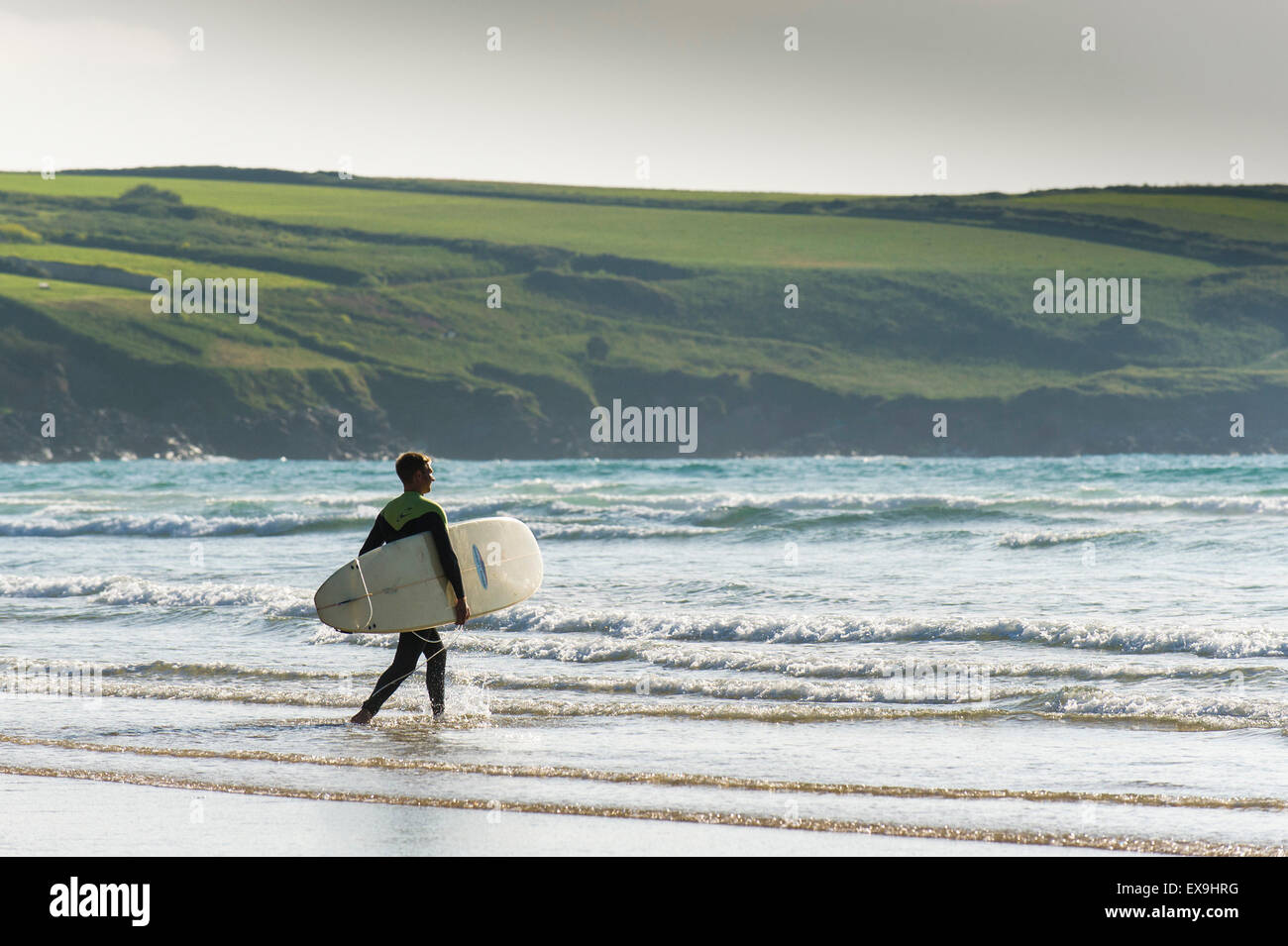 Un surfeur de marcher dans la mer à Crantock Beach à Newquay, Cornwall. Banque D'Images