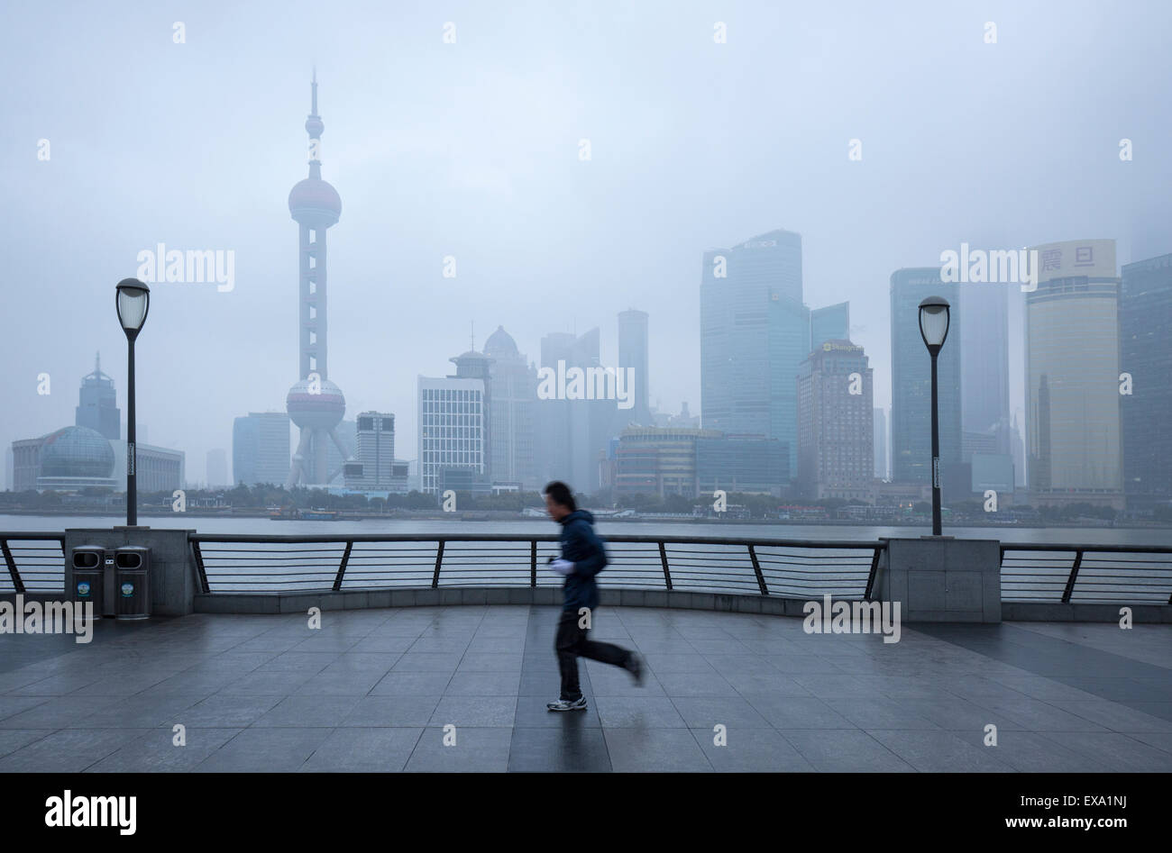 La Chine, Shanghai, Jogger passe devant l'horizon de Pudong District perdu dans les nuages bas le long de la rivière Huangpu sur matin d'hiver Banque D'Images