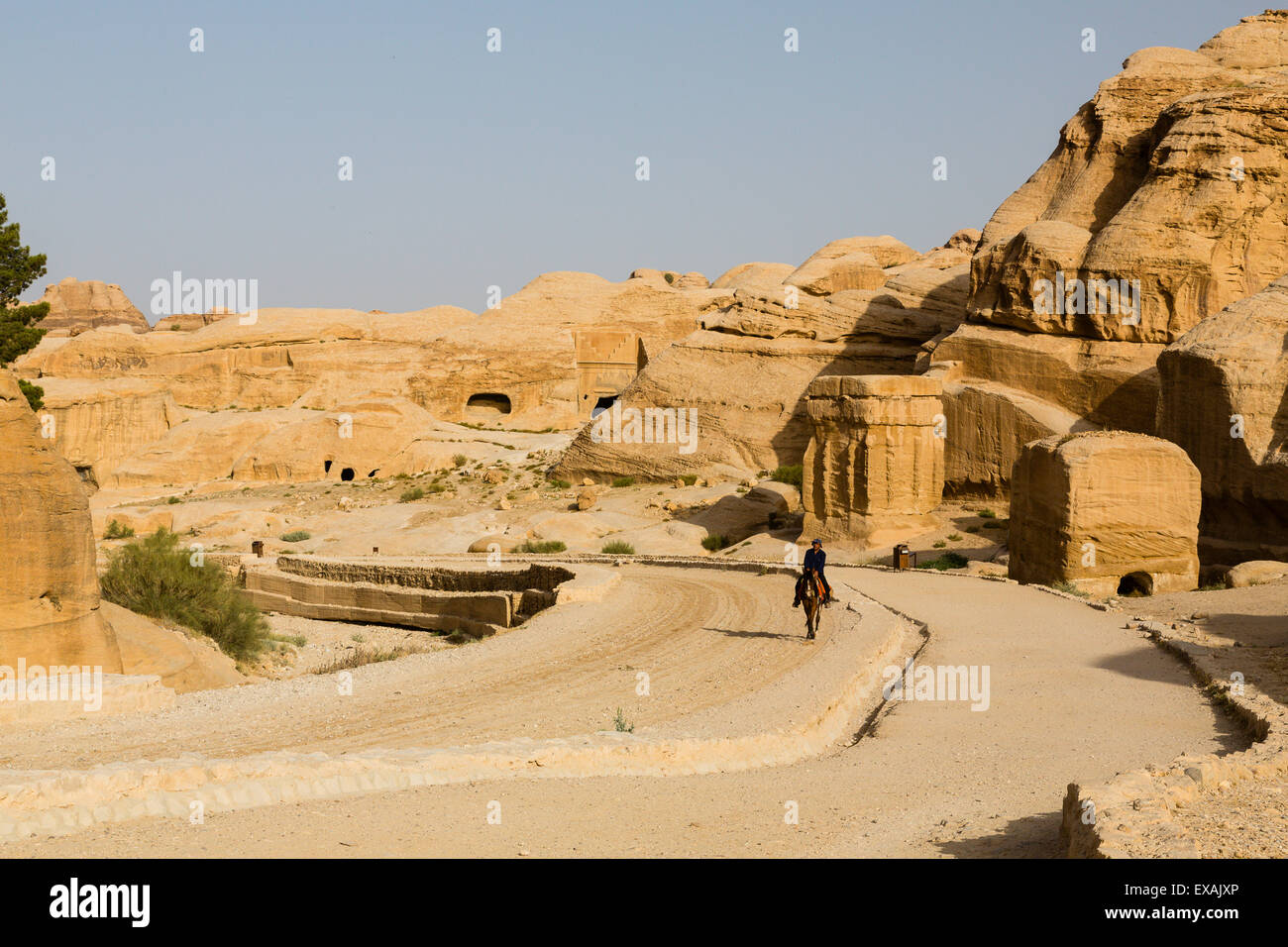 Petra, Jordanie. Un homme chevauche son cheval sculpté dans les bâtiments anciens en grès Petra contre un ciel bleu pâle. Banque D'Images