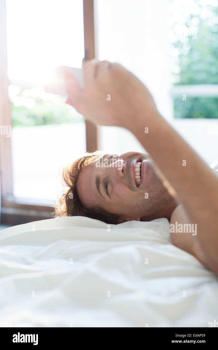 L'homme au lit en utilisant la messagerie instantanée pour smartphone multimédia Banque D'Images