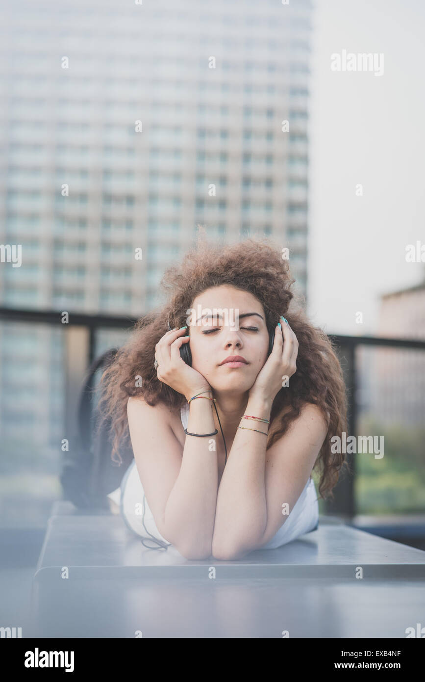 Belle jeune femme long cheveux bouclés hipster écoutez de la musique avec le comprimé dans la ville Banque D'Images