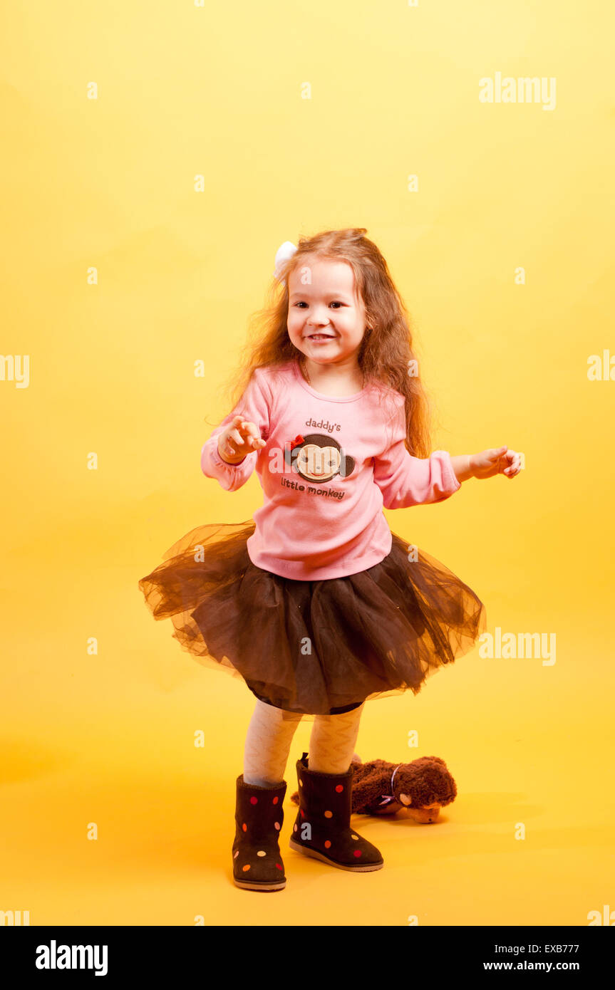 Jolie petite fille dansant dans une drôle de robe, studio photoshoot avec un fond jaune Banque D'Images