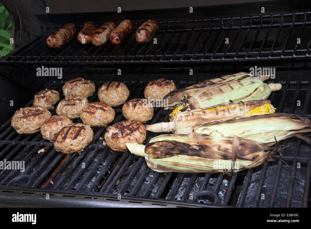 La cuisson des aliments sur un barbecue à gaz. Saucisses, hamburgers de dinde et de maïs prêt à manger Banque D'Images
