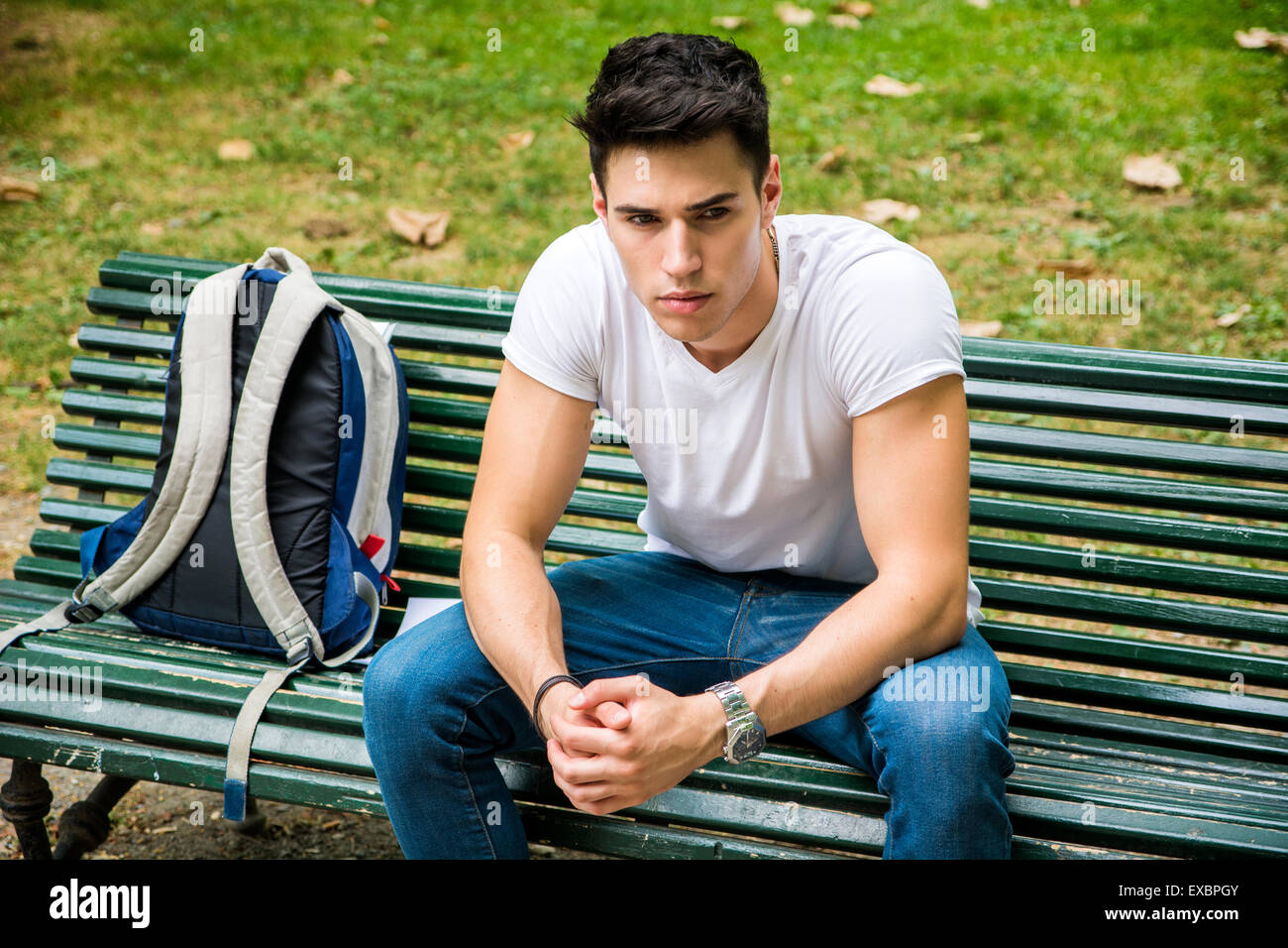 Jeune étudiant assis sur le banc dans un parc, à côté de son sac à dos, et tout en pensant à la suite au sérieux. Banque D'Images