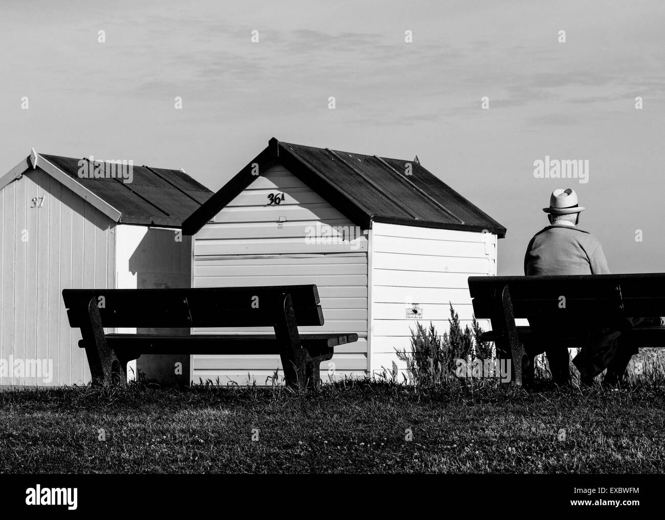 Image en noir et blanc homme mature homme assis par cabanes de plage Banque D'Images