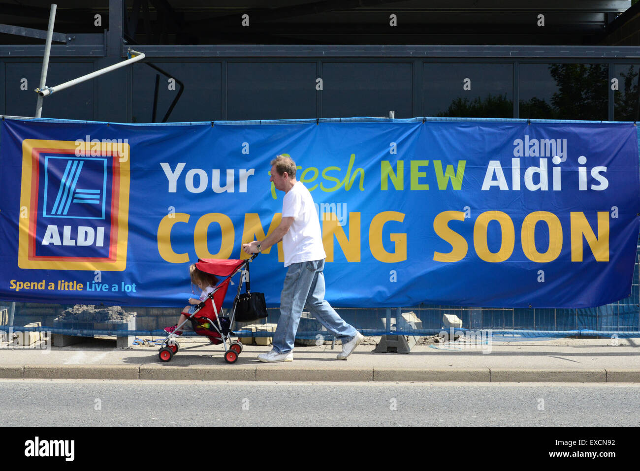 Un homme poussant un bébé dans une poussette passe devant un nouveau supermarché Aldi en construction. Photo : Scott Bairstow/Alamy Banque D'Images