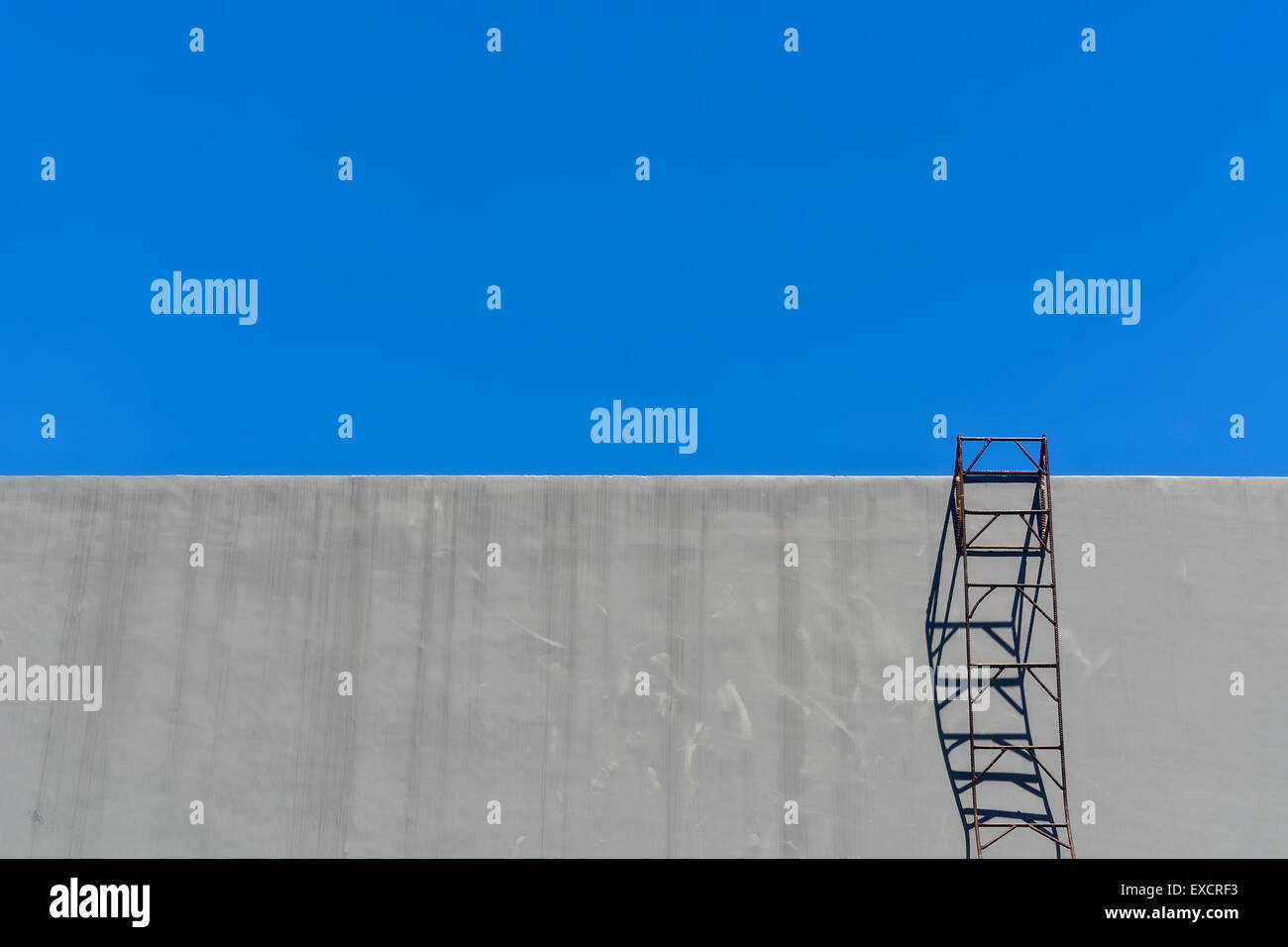 Sur l'échelle de l'acier contre mur gris ciel bleu sans nuages, Banque D'Images