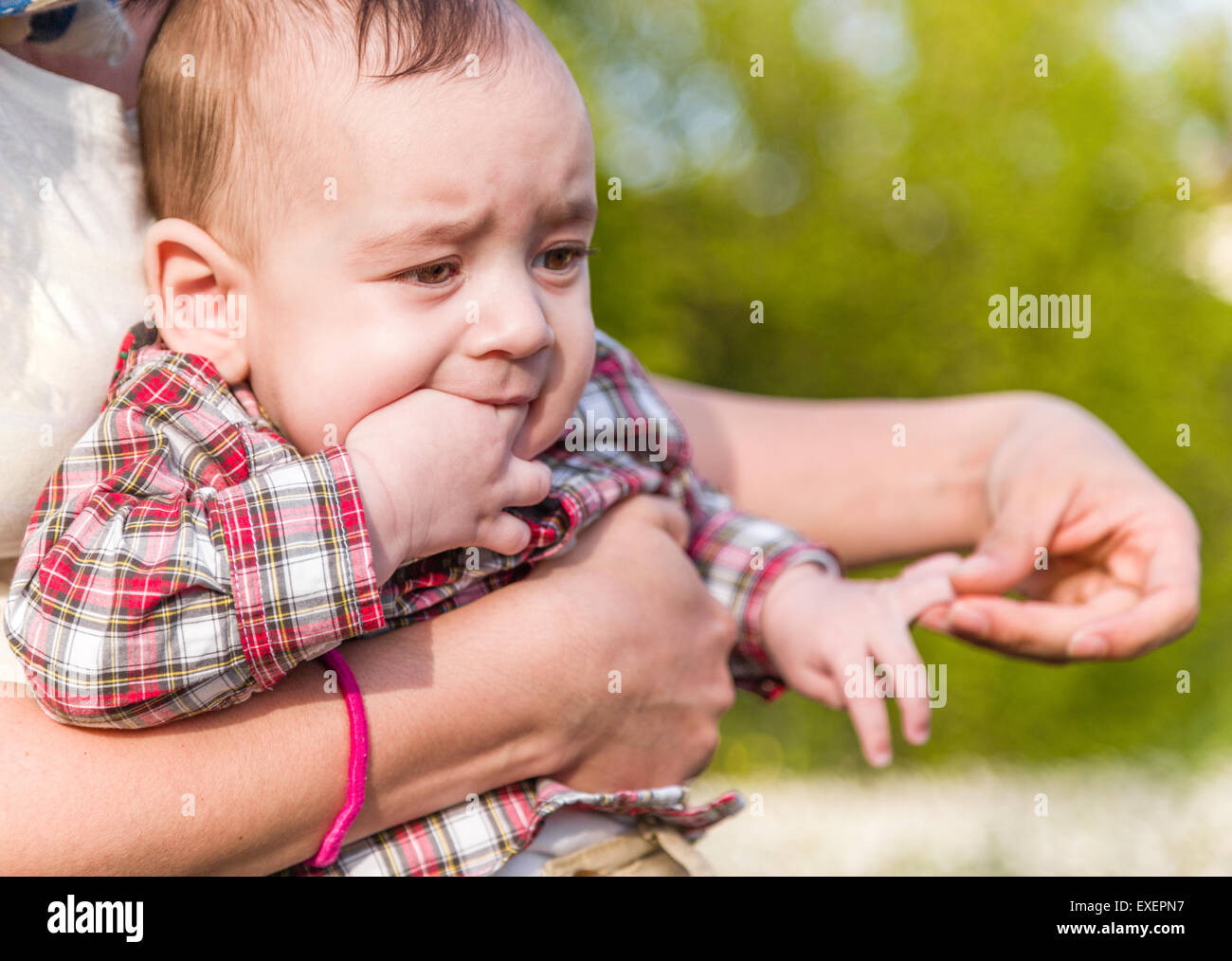 Mignon Bebe De 6 Mois Avec Les Cheveux Brun Clair A Rouge A Carreaux Chemise Et Pantalon Beige Est De Mordre Ses Doigts Tandis Que Embrasse Par Sa Mere Hispanique Photo Stock