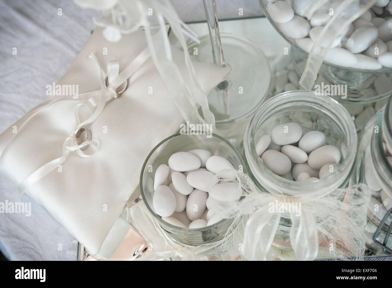 Dragée blanche dans des bocaux en verre avec paire de bagues de mariage Banque D'Images