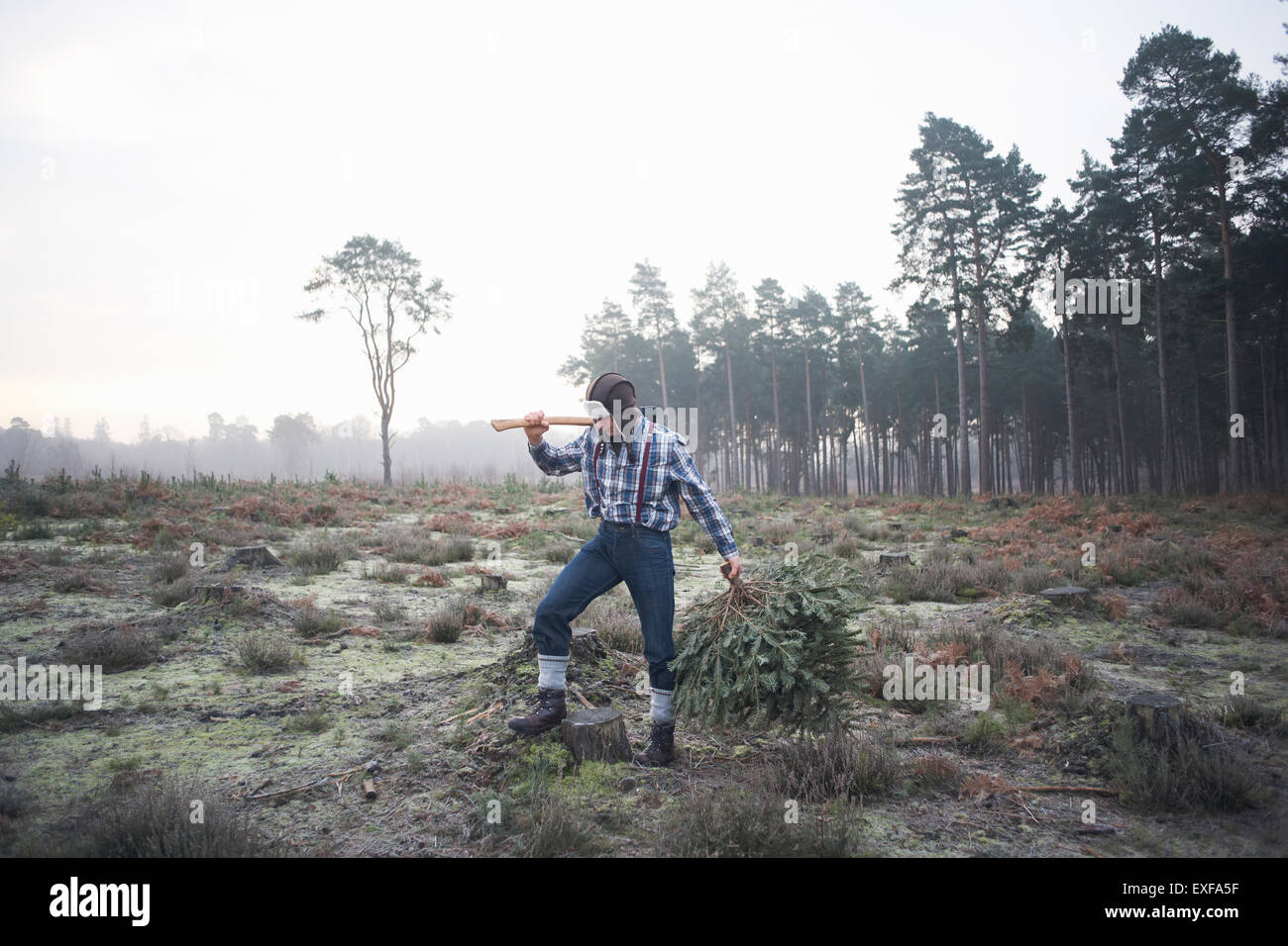 Woodsman matures debout dans le dégagement de forêt avec ax par-dessus son épaule Banque D'Images