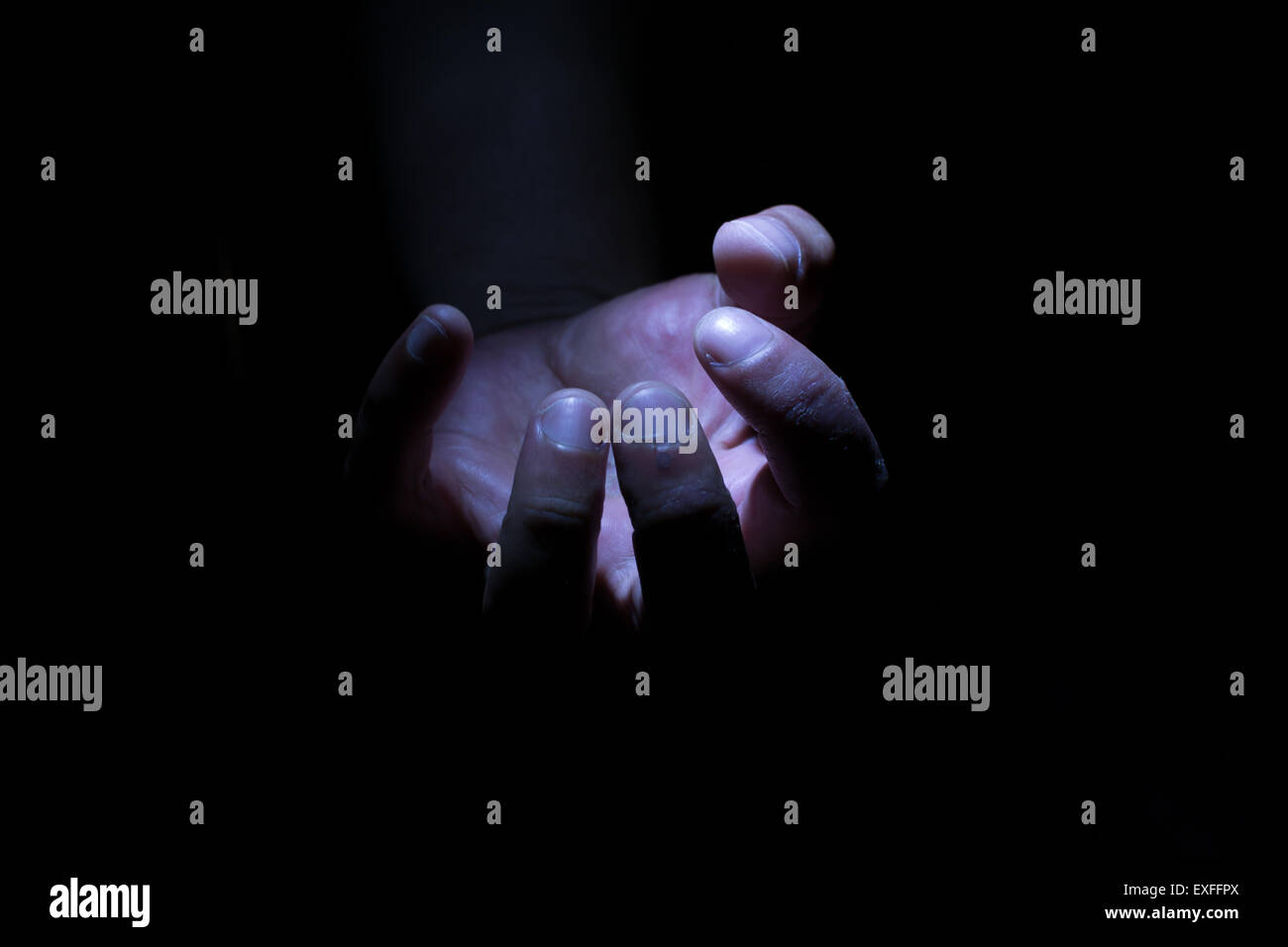 Homme de race blanche dans les ténèbres et l'ombre la main serrant un élément vide invisible Banque D'Images