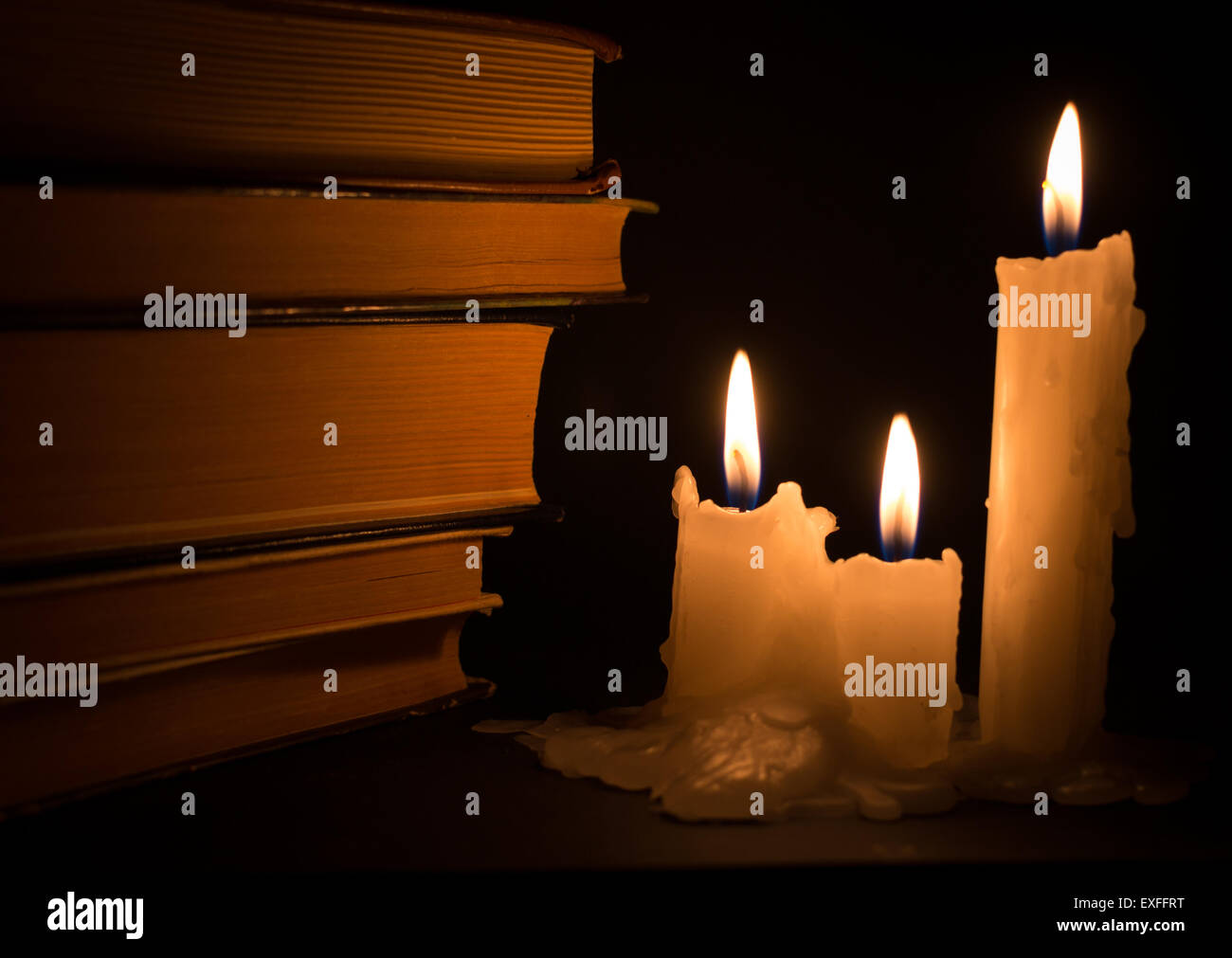 Trois bougies blanches des livres anciens de l'éclairage pendant l'obscurité de la nuit Banque D'Images