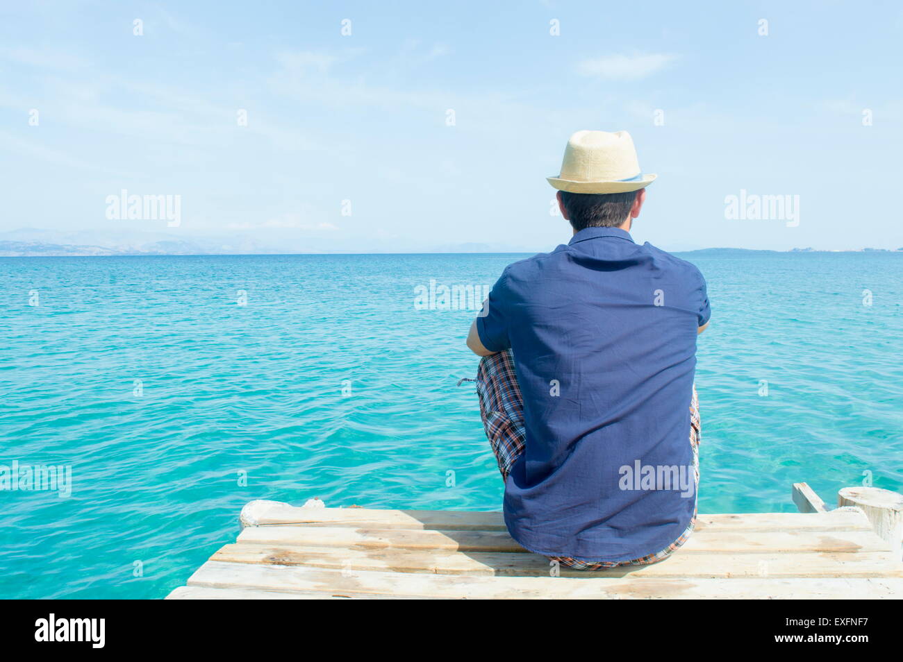 Jeune homme assis sur le quai et à la mer bleue à Banque D'Images