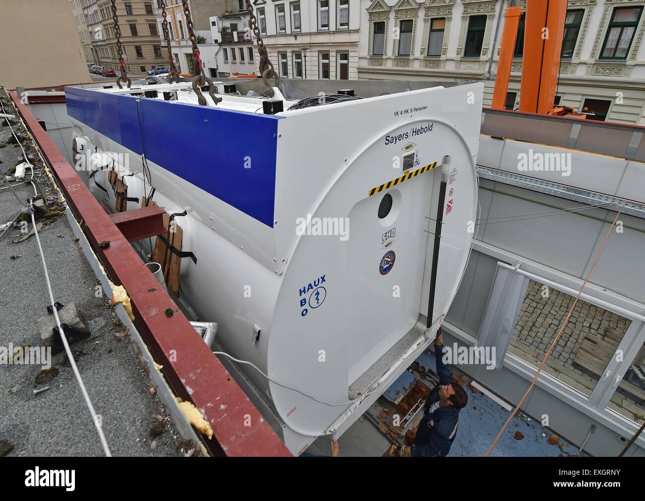 Employés d'une grue de levage de l'entreprise la chambre de pression de l'hôpital universitaire qui pèse 18 tonnes d'un bâtiment en extension Halle/Saale, Allemagne, 14 juillet 2015. Un camion à plateau se déplace la chambre de pression vers le nouveau bâtiment fonctionnel de l'hôpital, à six kilomètres de là, par la suite. La chambre est transférée dans le nouveau bâtiment, certains composants sont remplacés et dans six semaines, la chambre est de nouveau opérationnel. Ce qu'on appelle l'oxygénothérapie hyperbare (OHB) est un traitement médical de patients qui sont traités avec de l'oxygène pur à l'augmentation de la pression ambiante. Les patients qui souffrent de c Banque D'Images