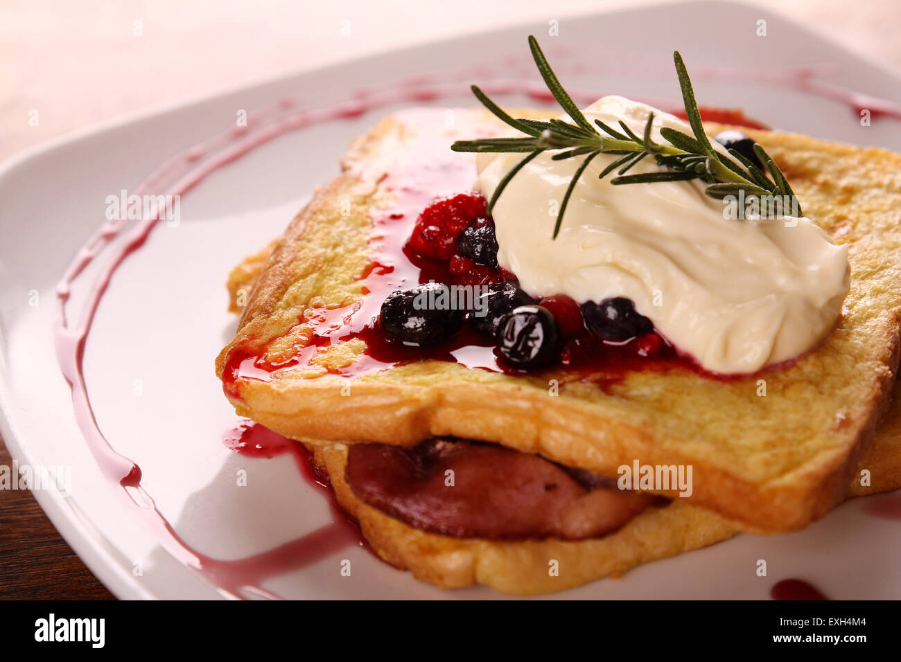 Délicieux pain doré au sirop de fruits rouges et crème de bacon sur une plaque blanche sur une table en bois. Banque D'Images