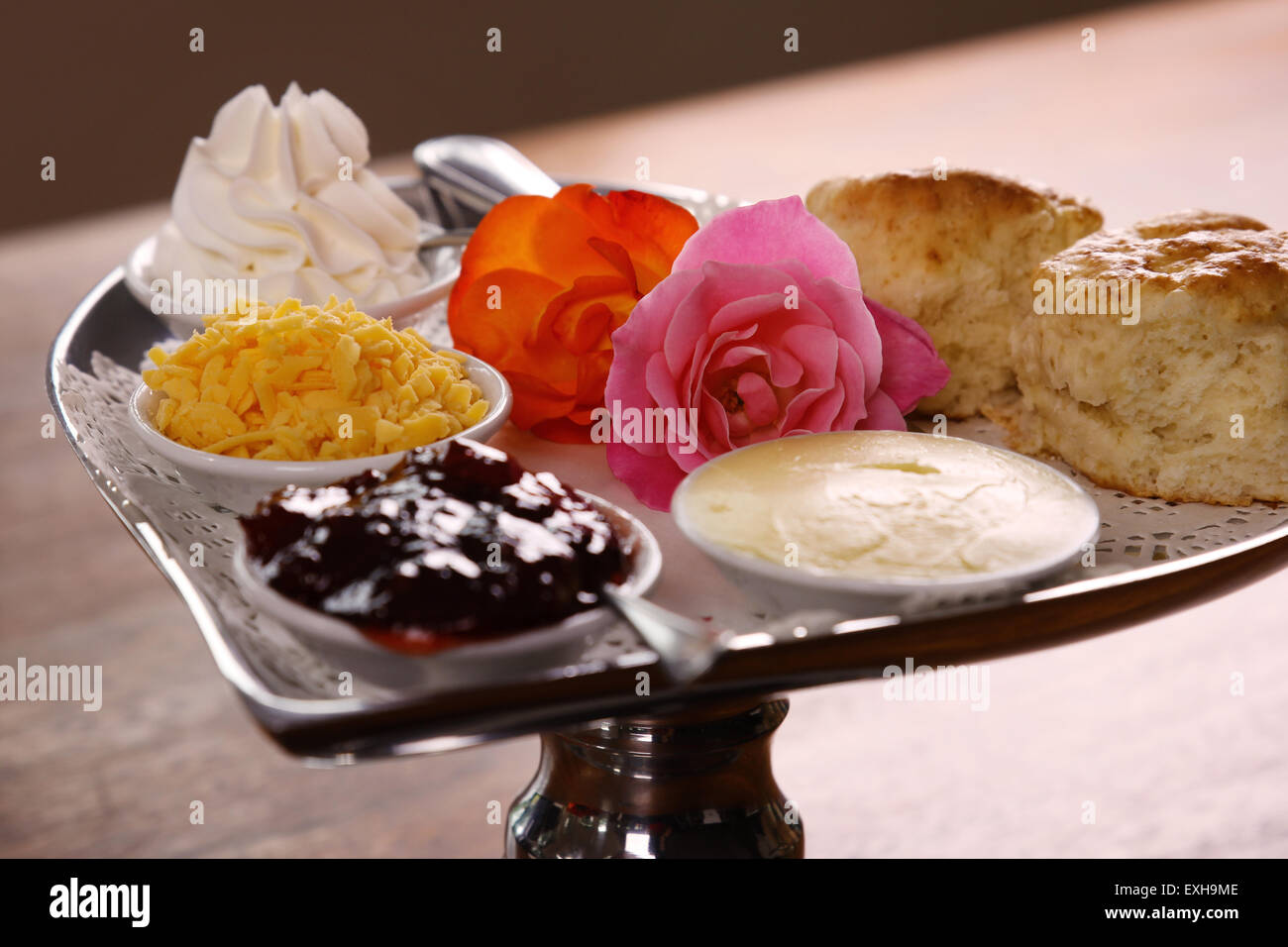 Délicieux scones beurre sur un plateau en forme de coeur argent servi avec du fromage et de la confiture de roses crème conserve sur une table en bois. Banque D'Images