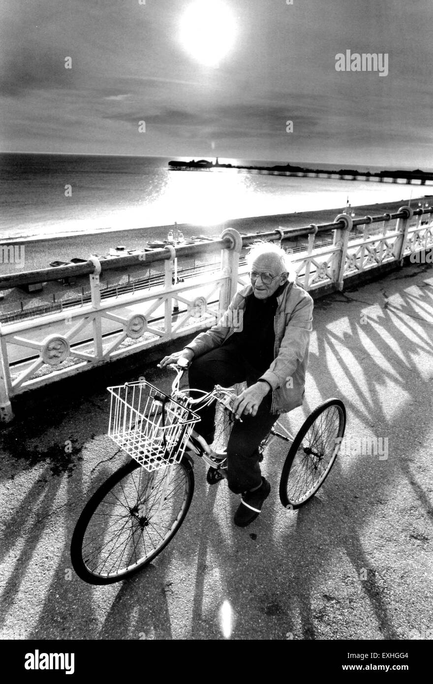 Vieil homme équitation son tricycle le long front de mer de Brighton 1990 que sun à propos de descendre Banque D'Images