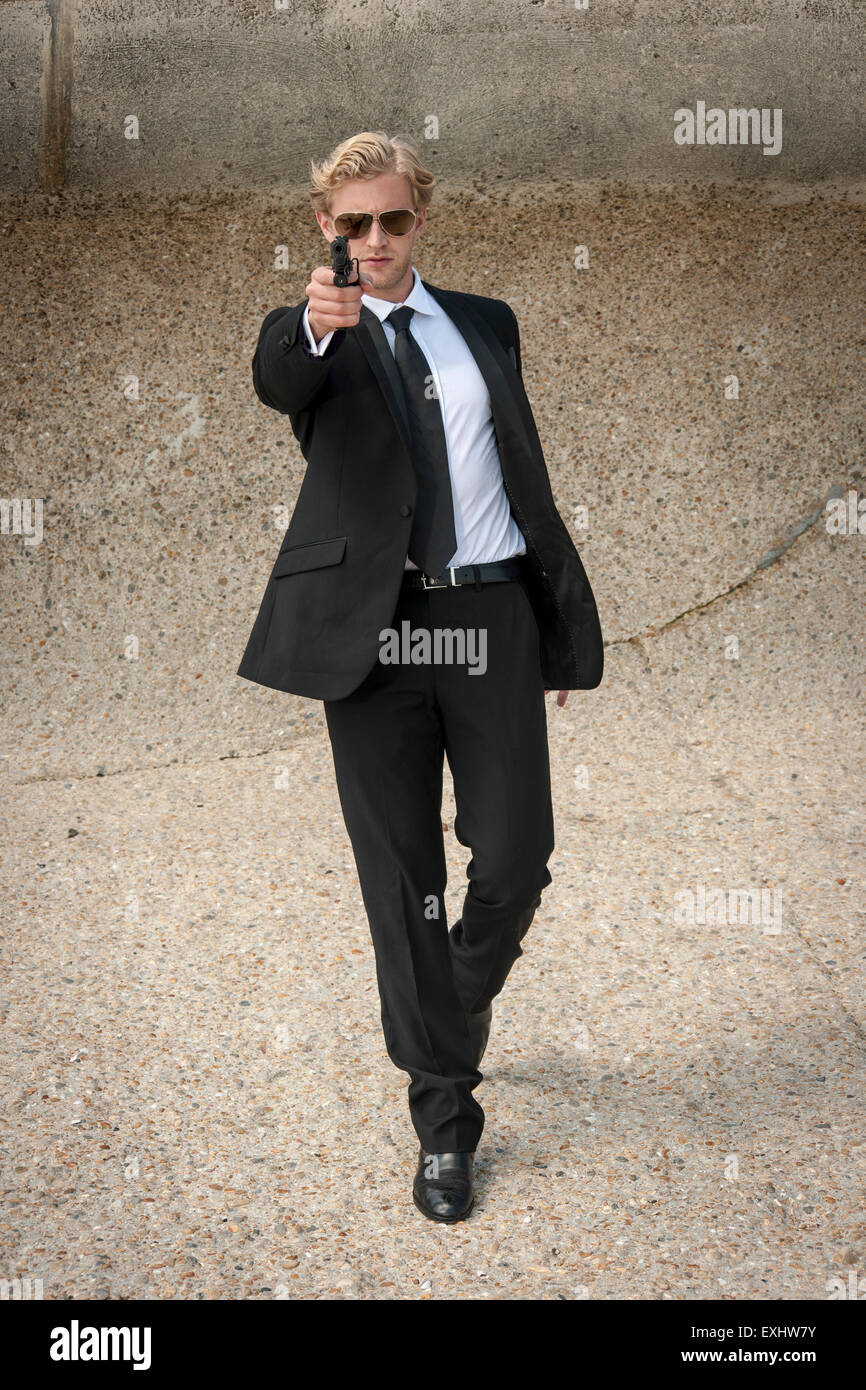 Homme marchant vers quelqu'un visant une arme à feu , prêt à tirer sur le port d'un costume noir. Banque D'Images