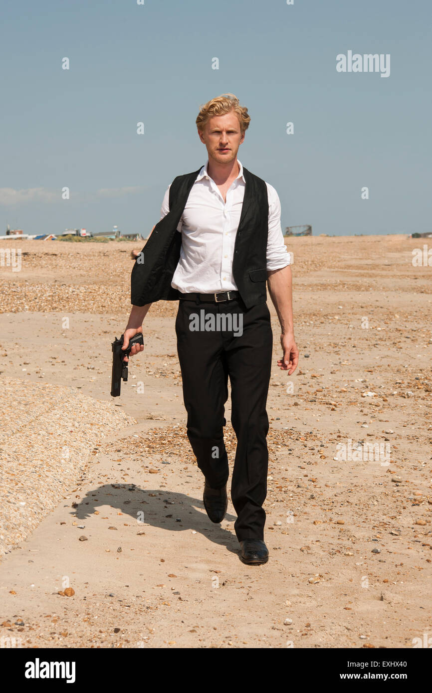 L'homme tenant un pistolet et une longue marche de la plage. Banque D'Images