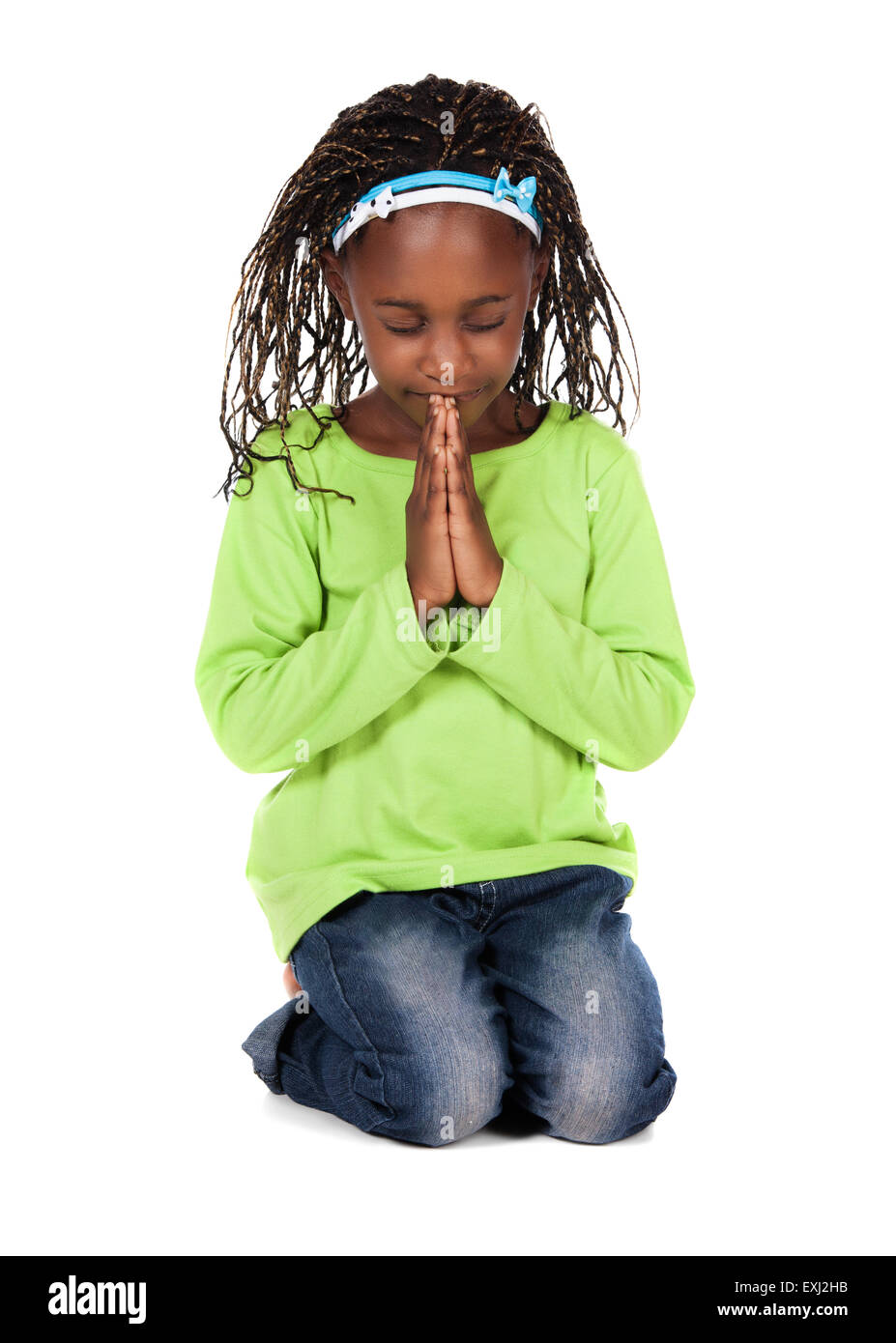 Adorable petit enfant africain avec tresses, portant un t-shirt vert et un jean bleu. La fille est à genoux et en priant. Banque D'Images