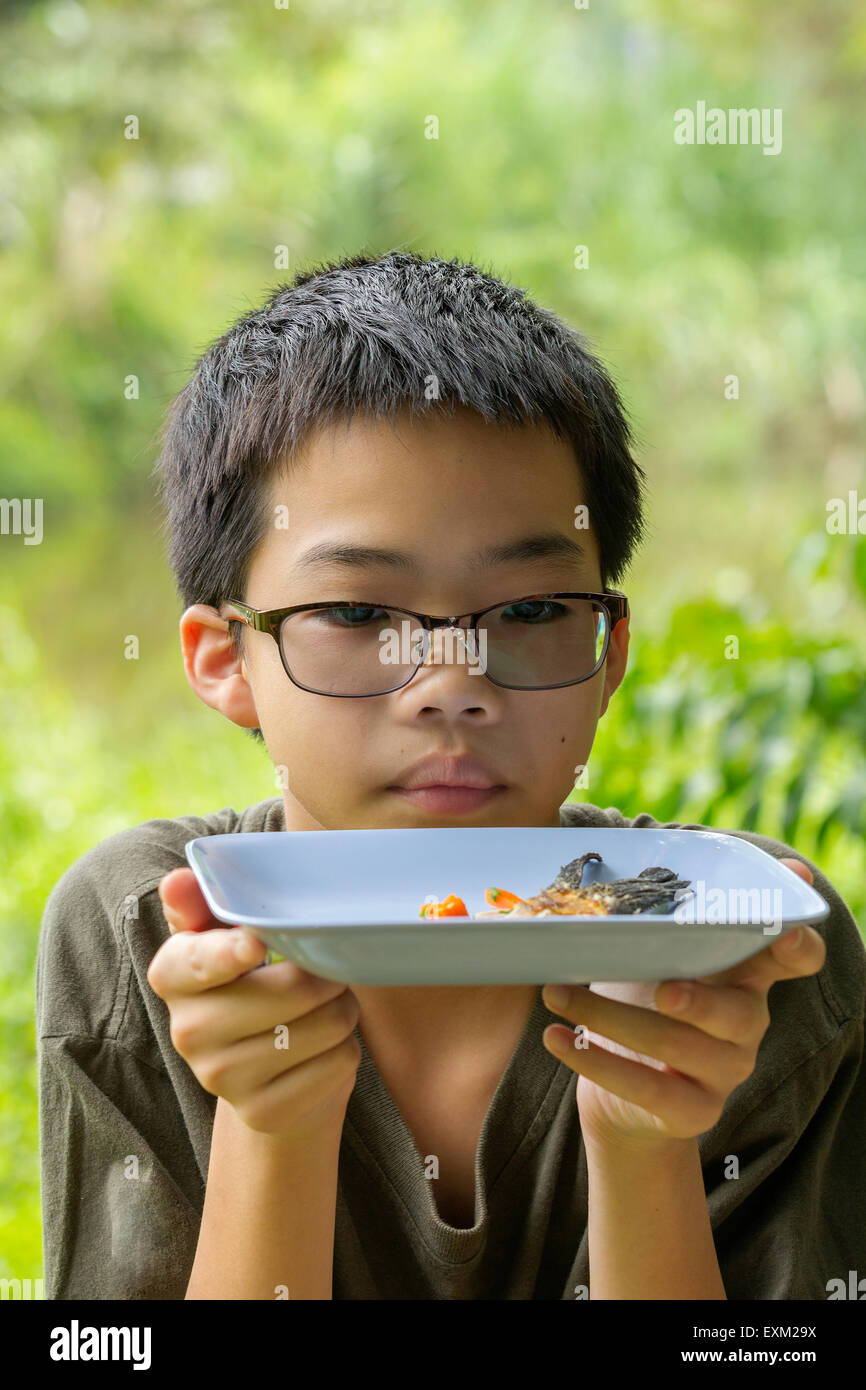 Portrait of Asian Thai pensive boy ressemble à de l'os de poisson poisson frit baret clairement mangé sur la plaque Banque D'Images