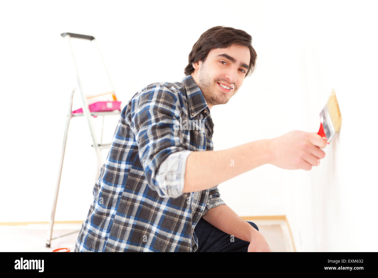 Vue d'un beau jeune homme peindre un mur dans son nouvel appartement Banque D'Images