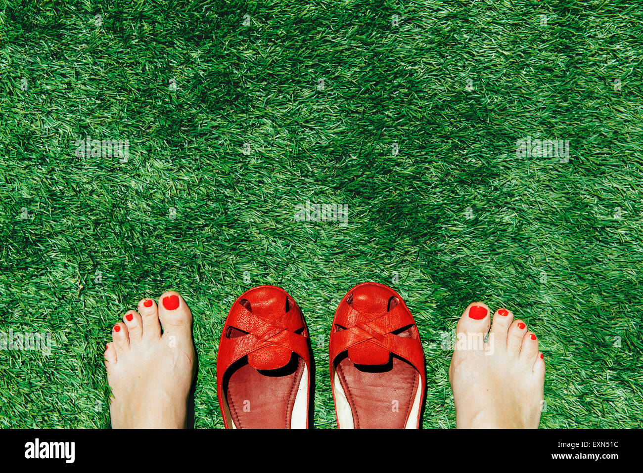 Les femmes aux pieds nus avec des ongles peints en rouge à côté d'une paire de chaussures rouges, sur l'herbe verte Banque D'Images