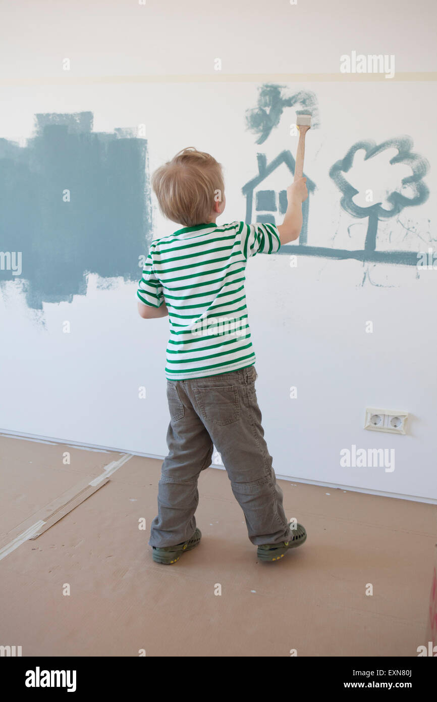 Petit garçon peinture Maison et arbre sur un mur de sa nouvelle chambre Banque D'Images