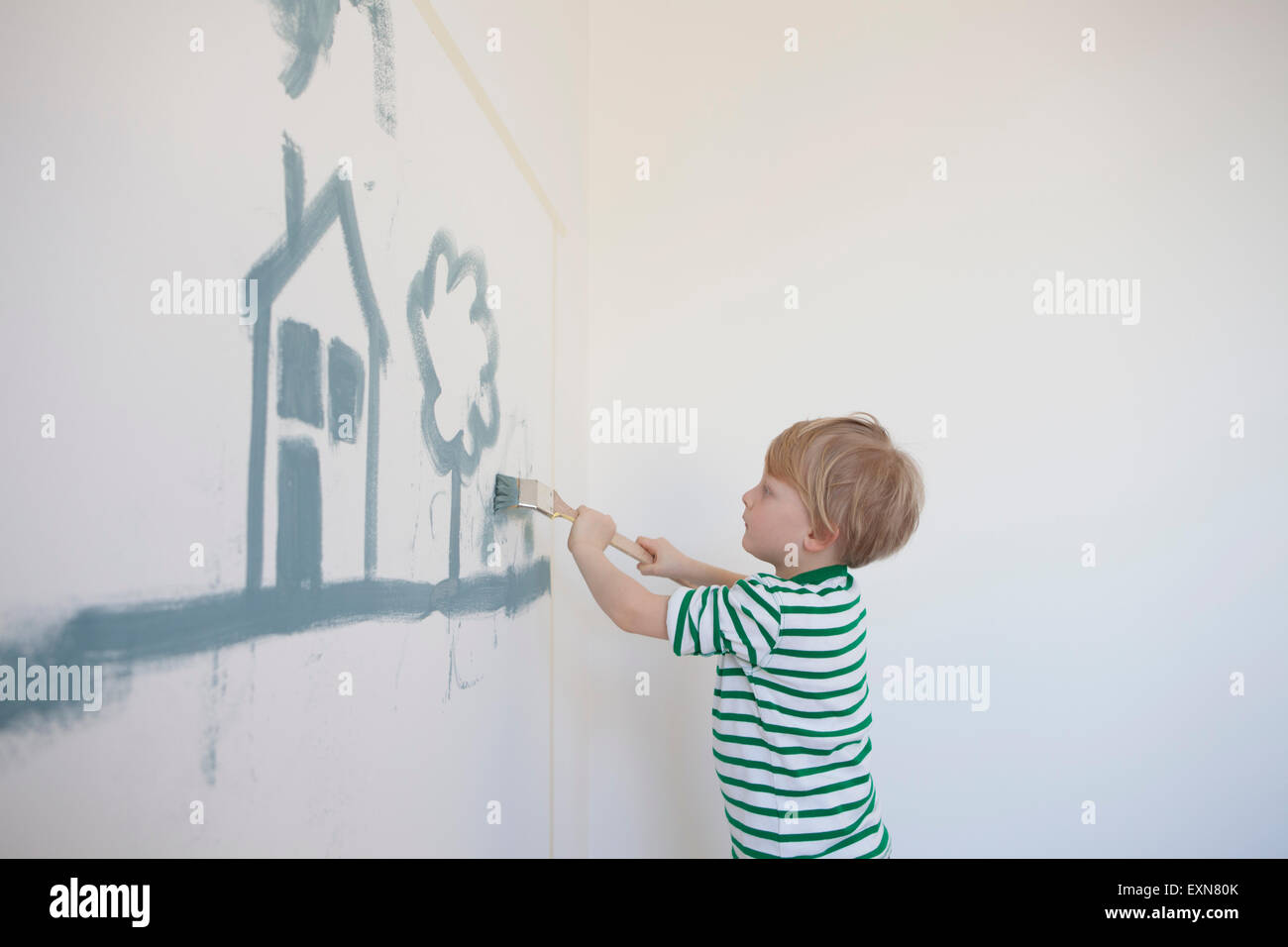 Petit garçon peinture Maison et arbre sur un mur de sa nouvelle chambre Banque D'Images