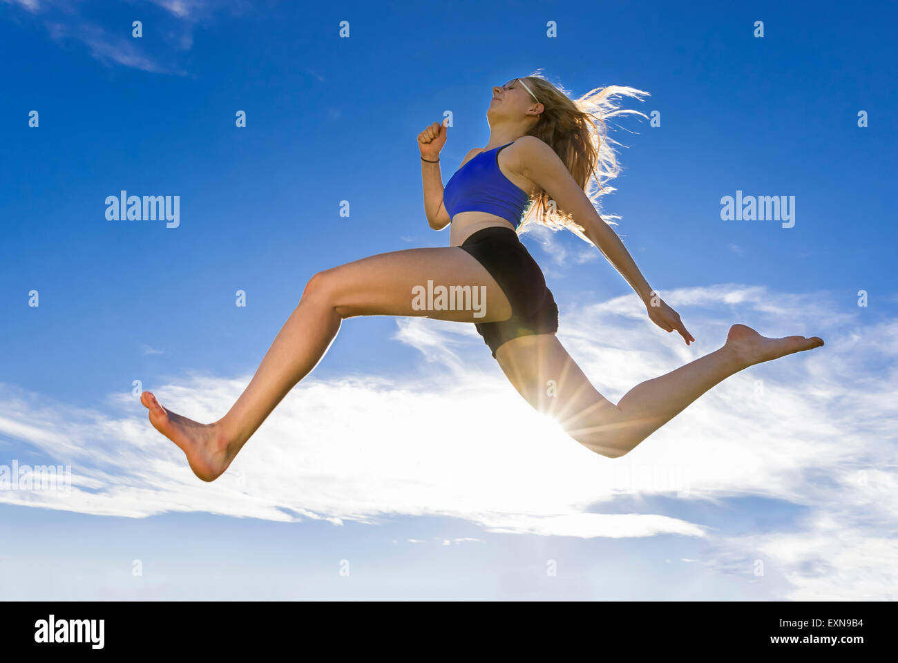 Jeune athlète sautant sous ciel bleu Banque D'Images