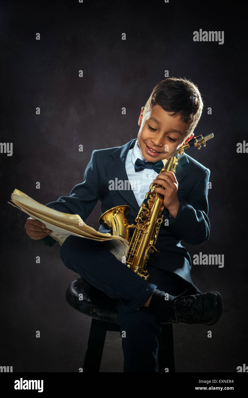 Un garçon de six ans s'asseoir avec le saxophone et la notation musicale lecture Banque D'Images