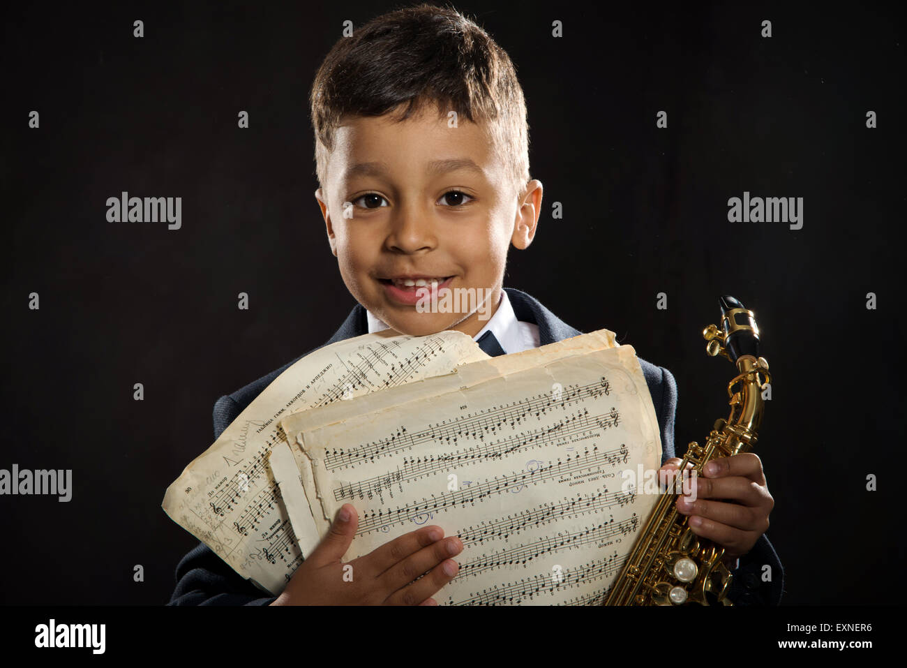 Un garçon de six ans s'asseoir avec le saxophone et sourire. close up portrait Banque D'Images