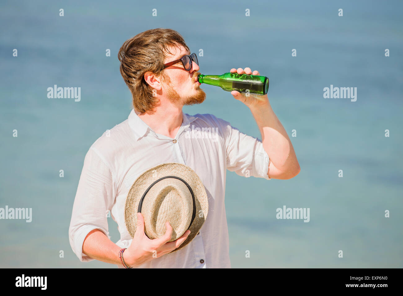 Homme portant un chapeau et des lunettes enjoing dans une bouteille de bière sur la plage Banque D'Images