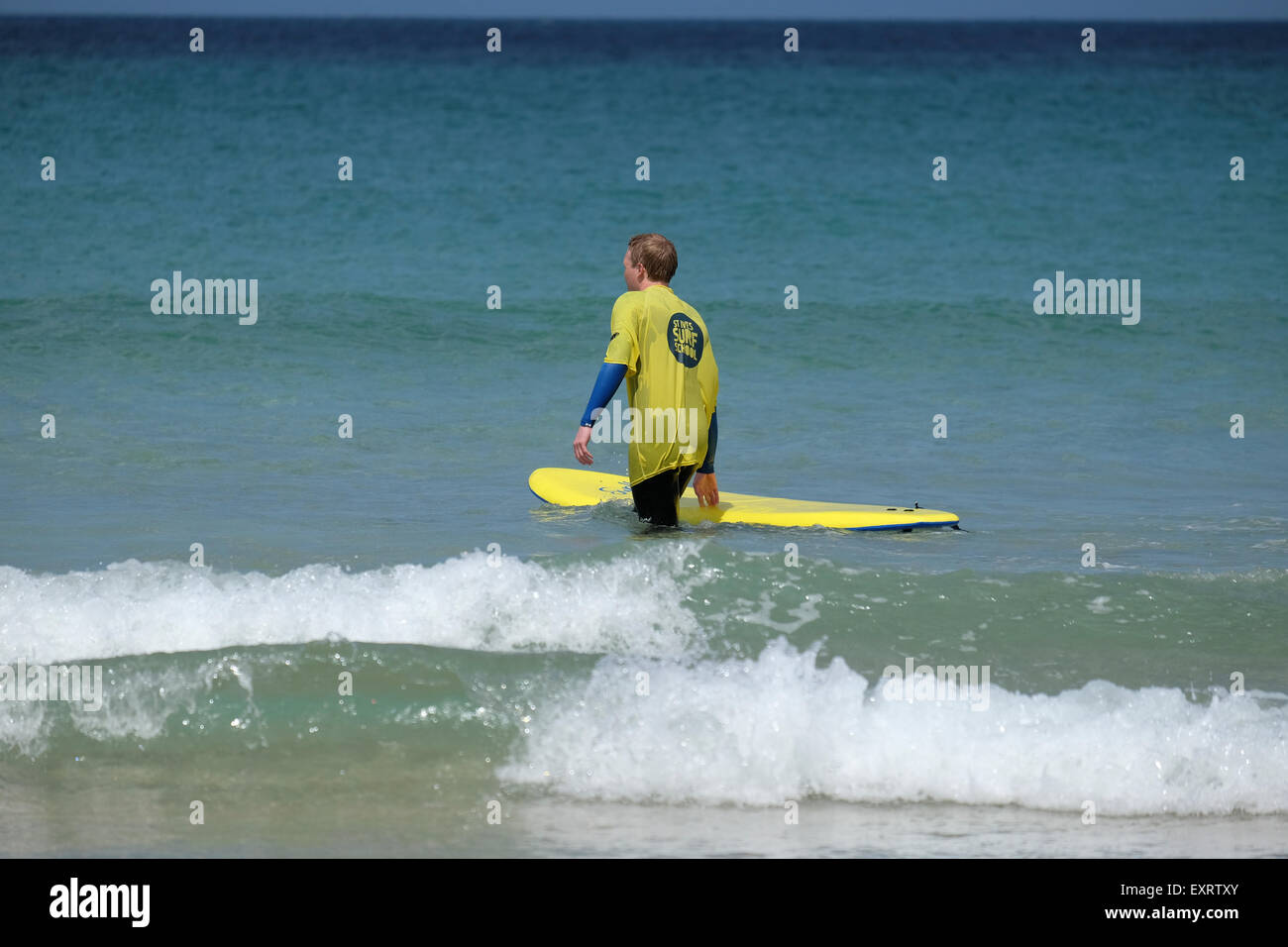 St Ives, Cornwall, UK : l'homme en jaune Surf School T-shirt dans l'eau, apprendre à surfer sur la plage de Porthmeor à St Ives dans Banque D'Images