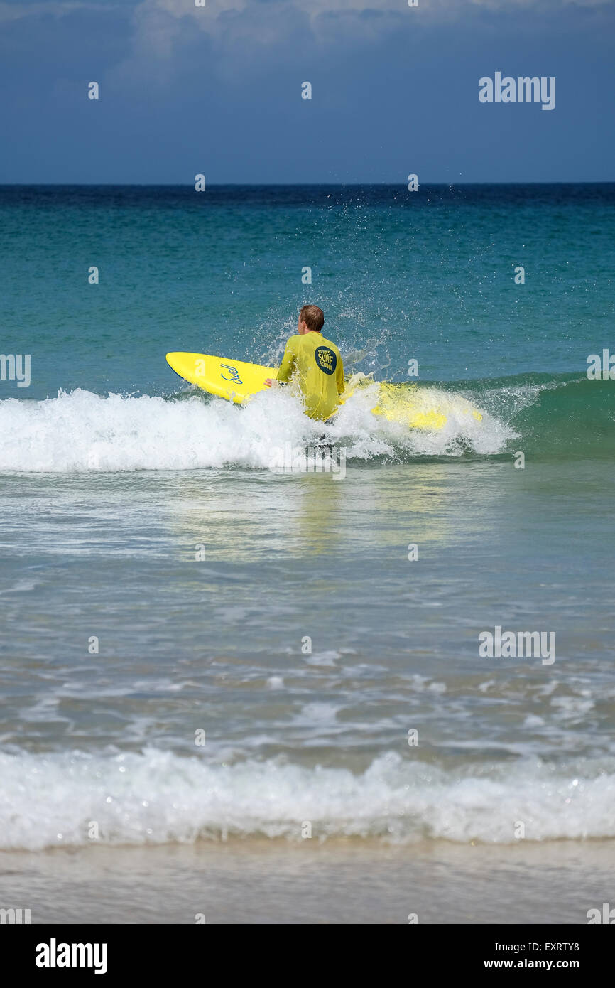 St Ives, Cornwall, UK : l'homme en jaune Surf School T-shirt dans l'eau, apprendre à surfer sur la plage de Porthmeor à St Ives dans Banque D'Images