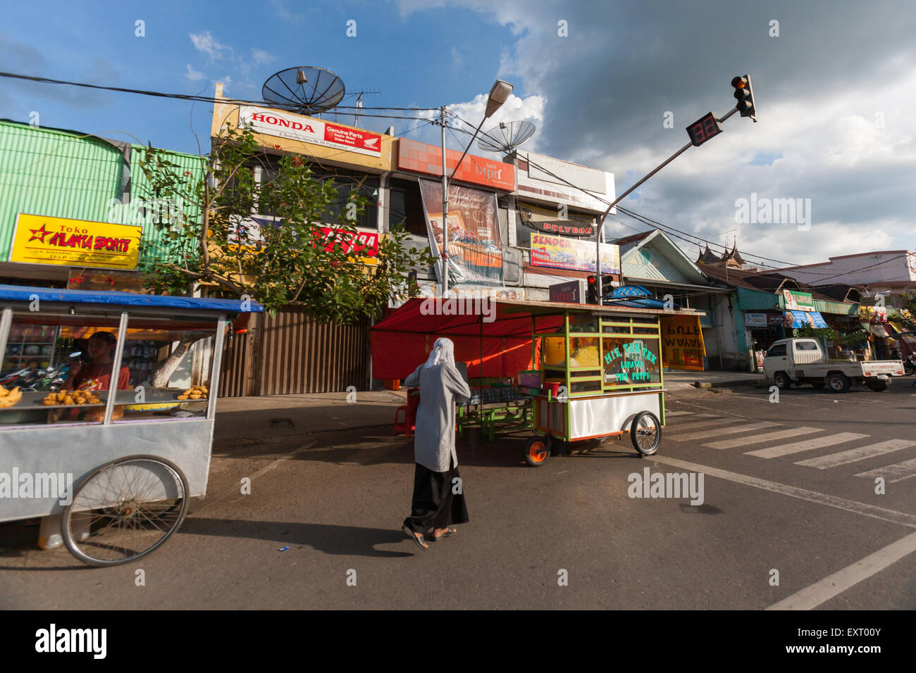 Une femme qui marche sur la route, passe devant des vendeurs de nourriture de rue à Payakumbuh, Sumatra Ouest, Indonésie. Banque D'Images