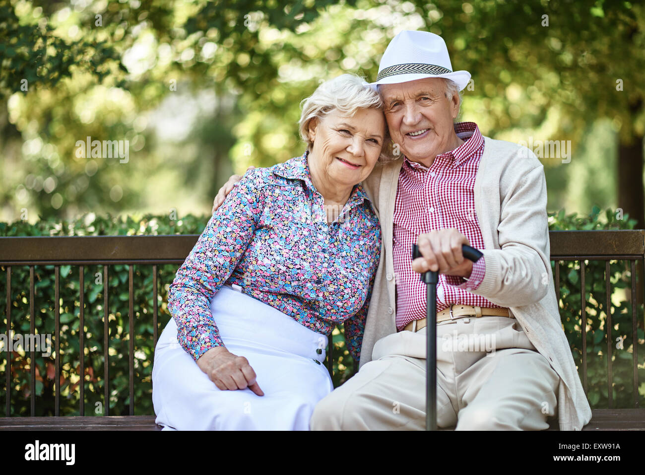 Senior couple sitting on bench in park et looking at camera Banque D'Images