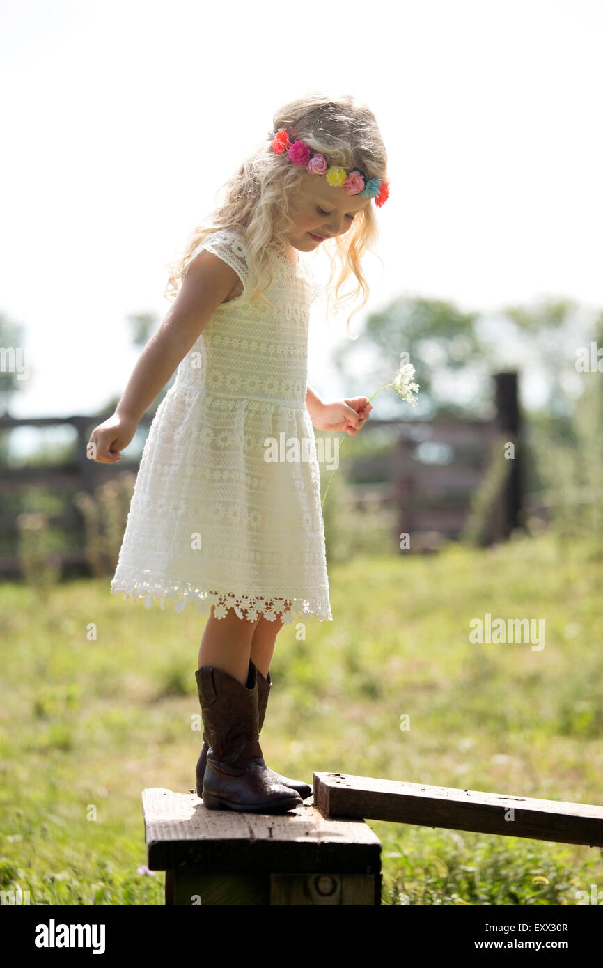 Cute girl (4-5) in white dress debout sur une clôture en prairie Banque D'Images