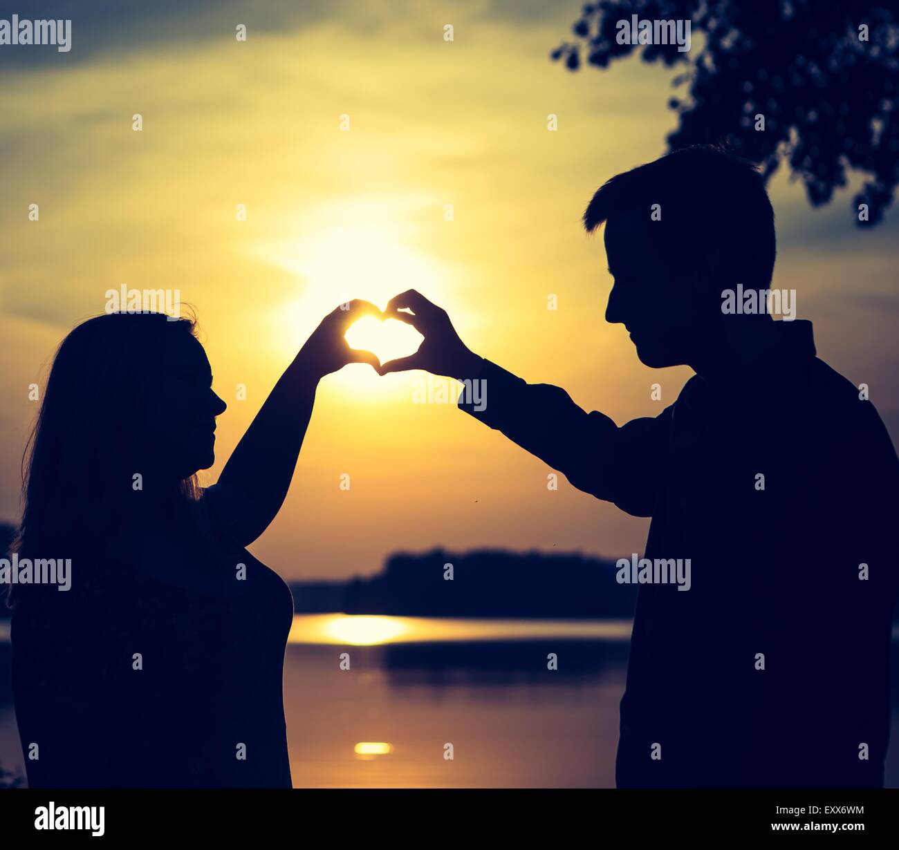 Couple forme de cœur avec leurs mains sur les rives du lac. Les gens silhouettes vintage photo. Banque D'Images