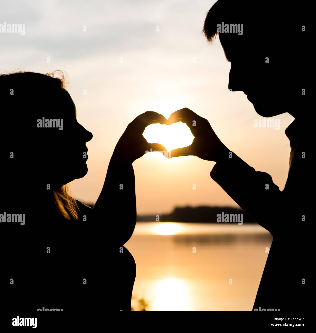 Couple forme de cœur avec leurs mains sur les rives du lac. Les gens silhouettes vintage photo. Banque D'Images