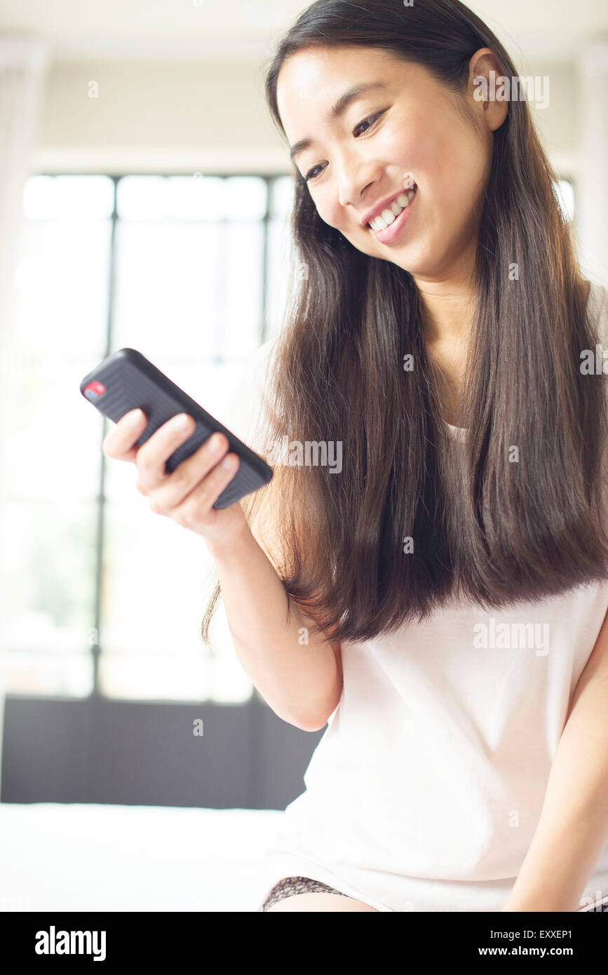 Woman sitting in bed using smartphone Banque D'Images