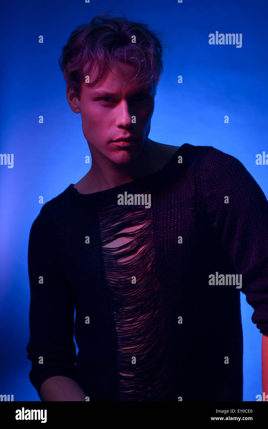 Un jeune homme de race blanche model posing, un moody high fashion portrait faiblement éclairé en rose et concept la lumière bleue. Banque D'Images