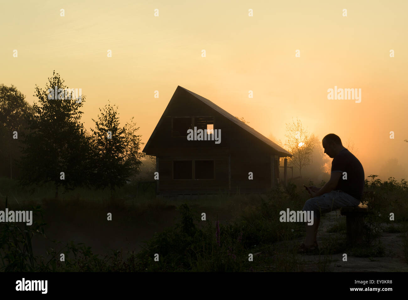 L'homme avec téléphone tôt le matin reste à la maison sur la rive d'un étang Banque D'Images