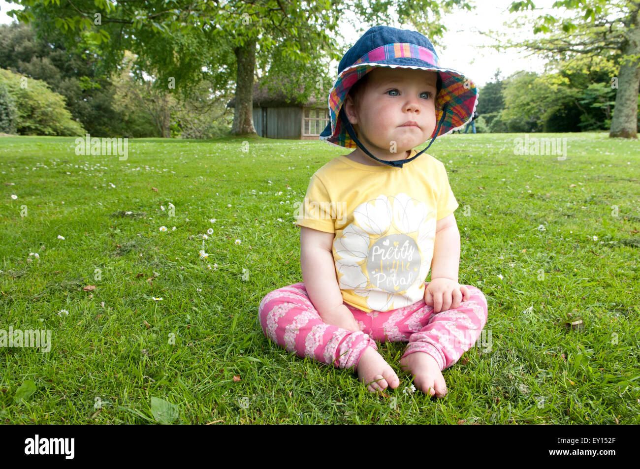 Petite fille assise sur l'herbe portant un chapeau de soleil à réfléchi Banque D'Images