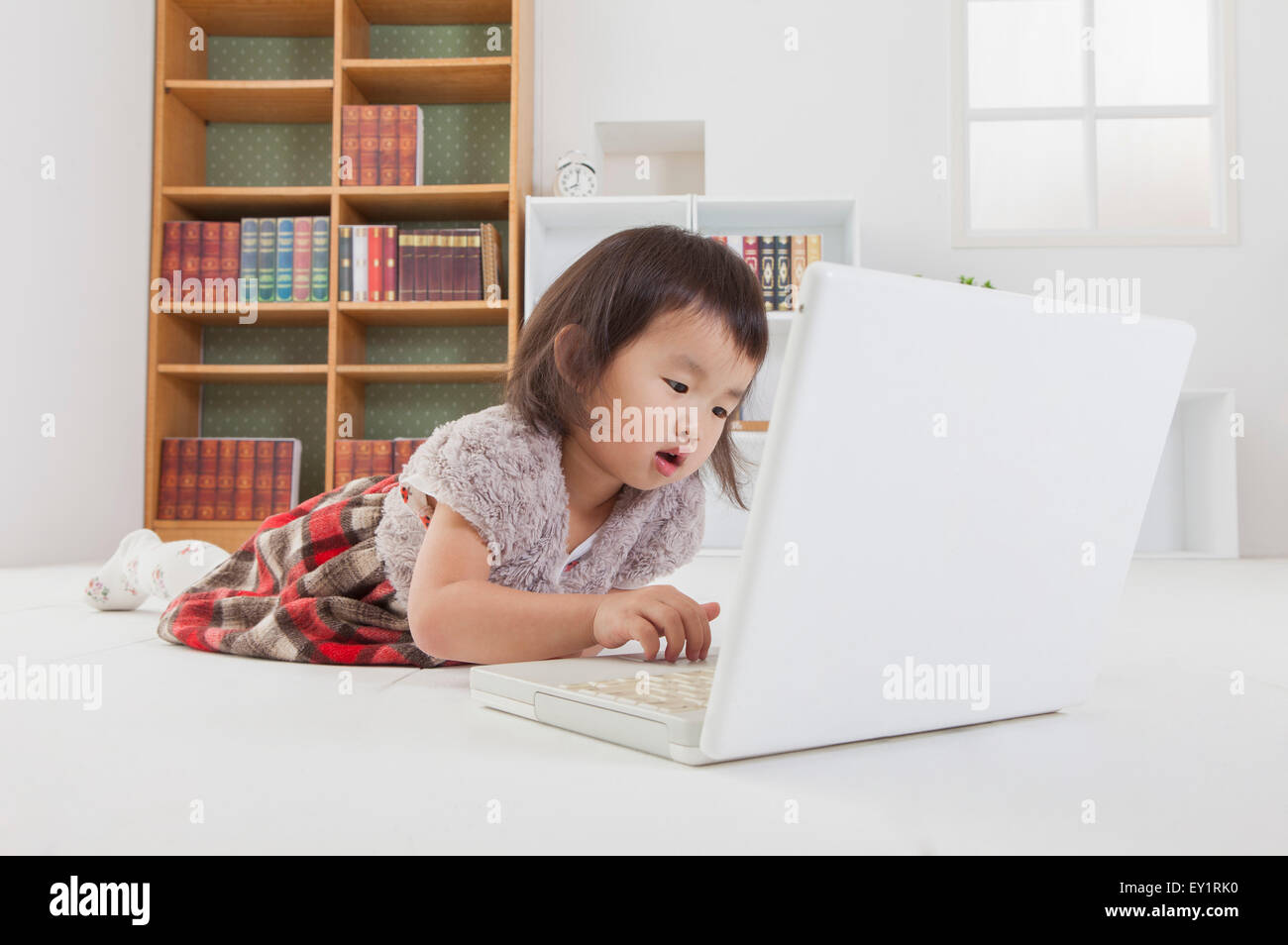 Petite fille couchée sur l'avant et jouer avec un ordinateur portable, Banque D'Images