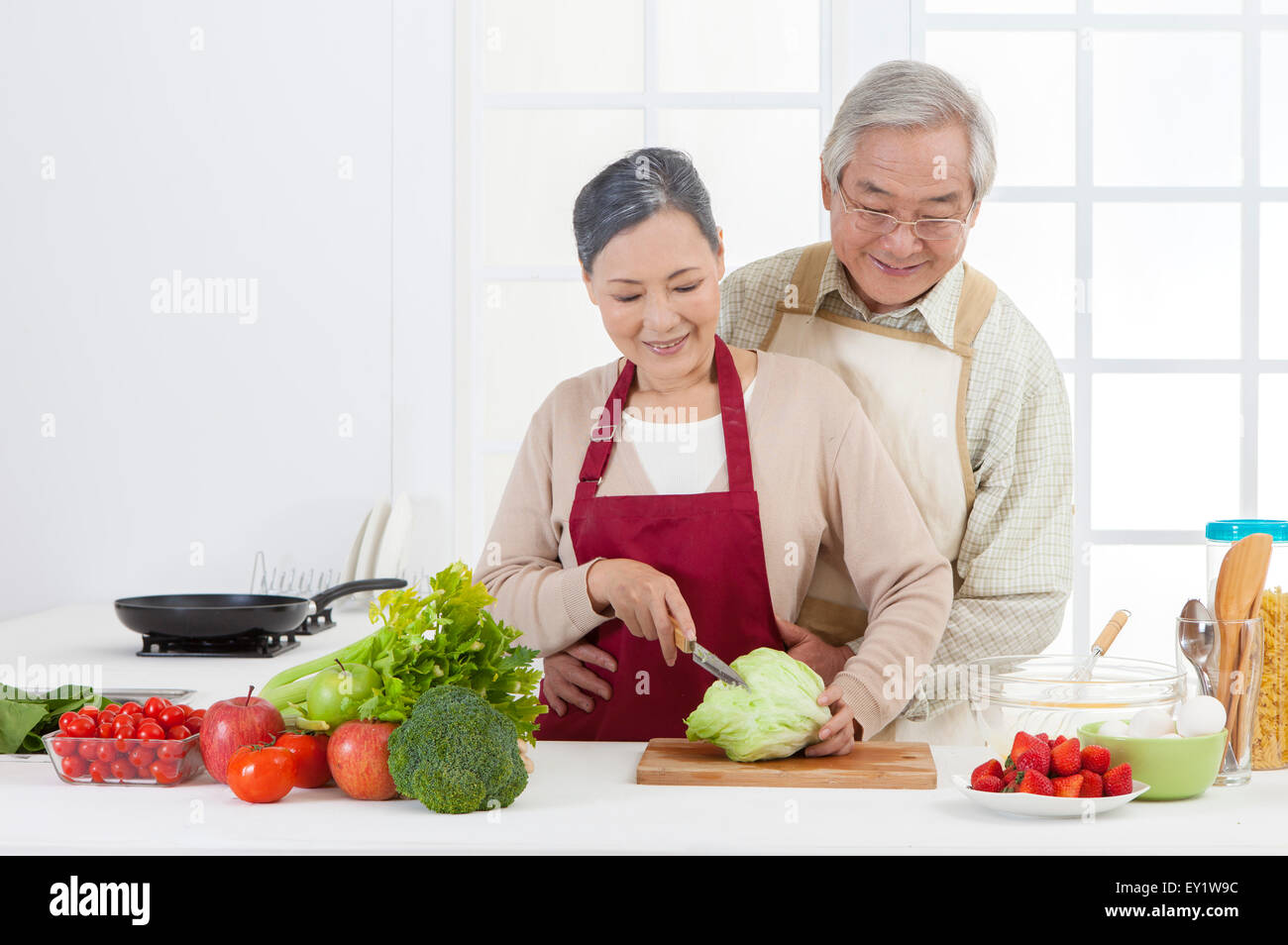 Senior couple couper des légumes dans la cuisine et sourit joyeusement, Banque D'Images