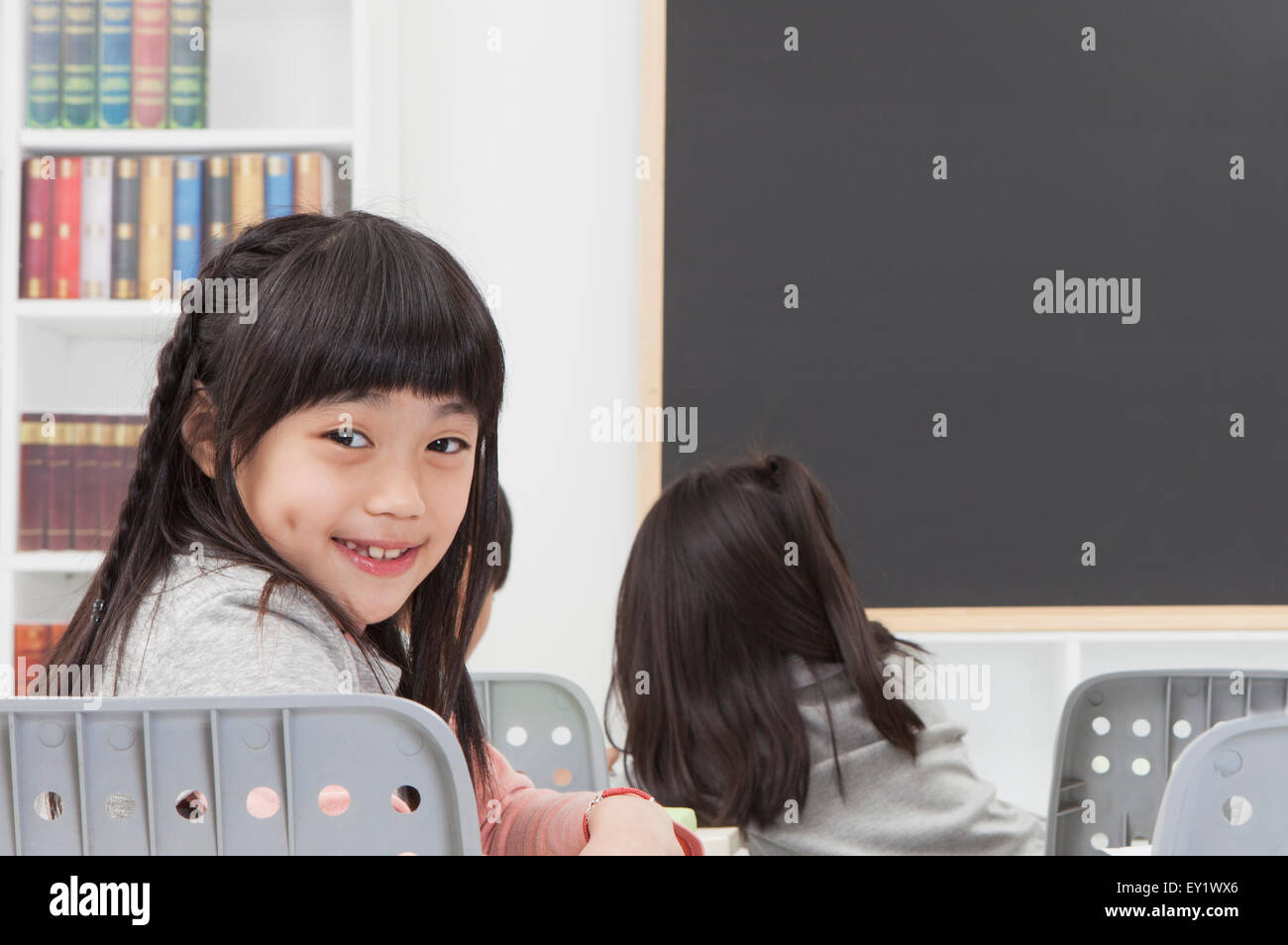 Fille assise dans la salle de classe et souriant à la caméra, Banque D'Images