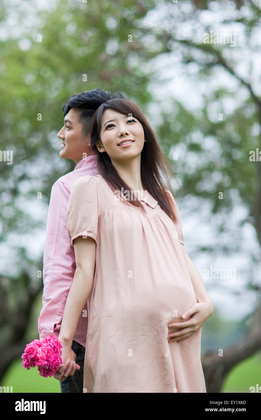 Femme enceinte et jeune homme debout avec dos à dos et holding Flowers avec sourire, Banque D'Images