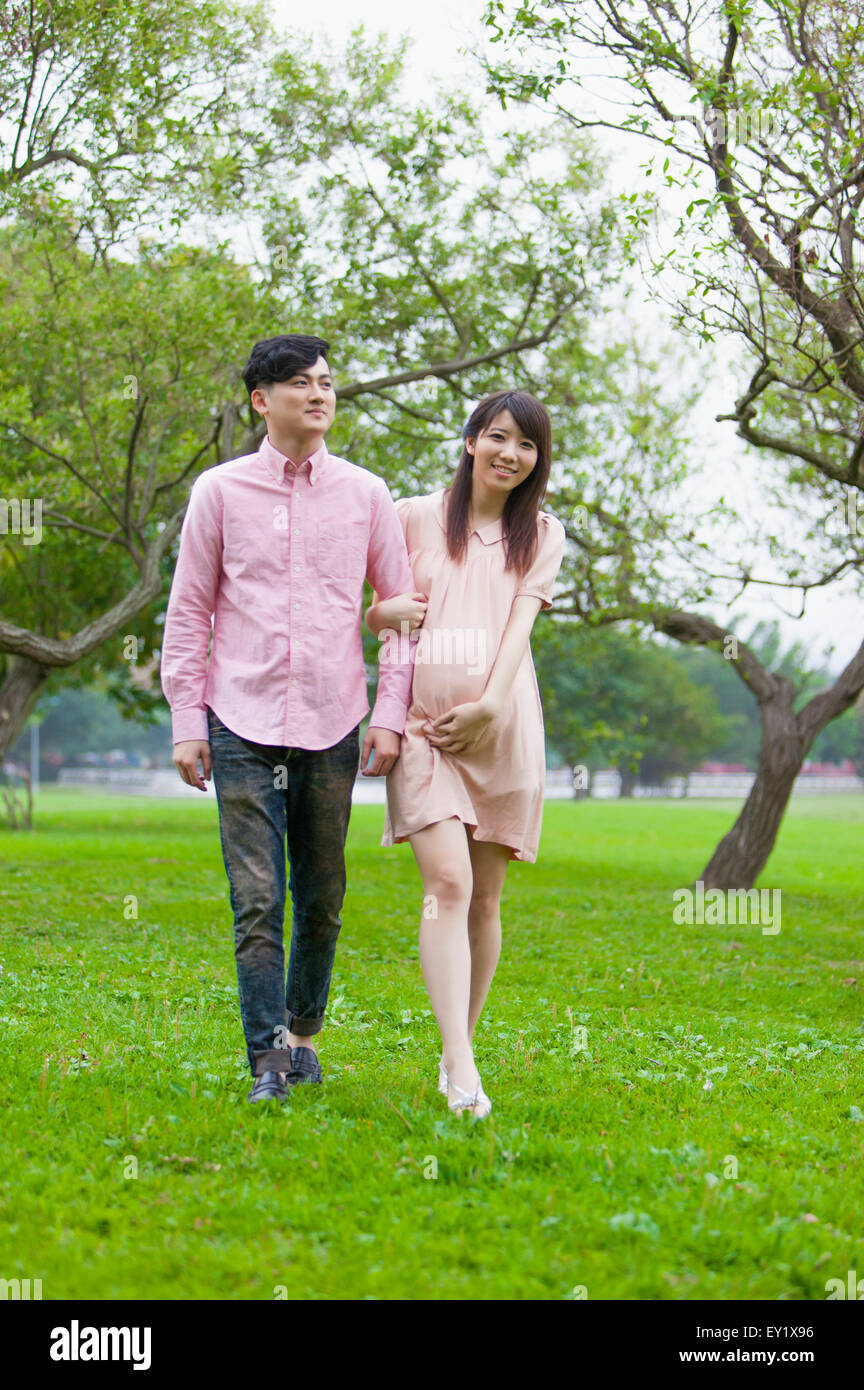 Jeune homme et femme enceinte marche sur la pelouse et à l'écart avec sourire, Banque D'Images